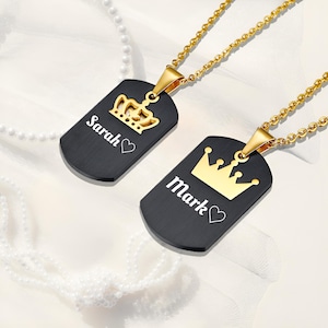 Puede incluir: Dos collares con medallas de perro de metal negro y cadenas doradas. Las medallas tienen una corona y los nombres "Sarah" y "Mark" grabados.