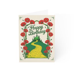 May include: A folded birthday card with a whimsical design. The card features a yellow brick road leading to a green castle, framed by red poppies. The words "Happy Birthday" are written in green script.