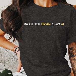 May include: A dark grey t-shirt with the text "MY OTHER BRAIN IS AN AI" in white and yellow lettering.