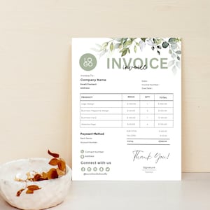 Könnte beinhalten: Eine weiße Rechnung mit grünen floralen Akzenten und dem Wort "INVOICE" oben. Die Rechnung enthält Abschnitte für Unternehmensinformationen, Produktdetails und eine "Thank You!"-Nachricht. Eine kleine Schale mit getrockneten Blättern befindet sich im Vordergrund.