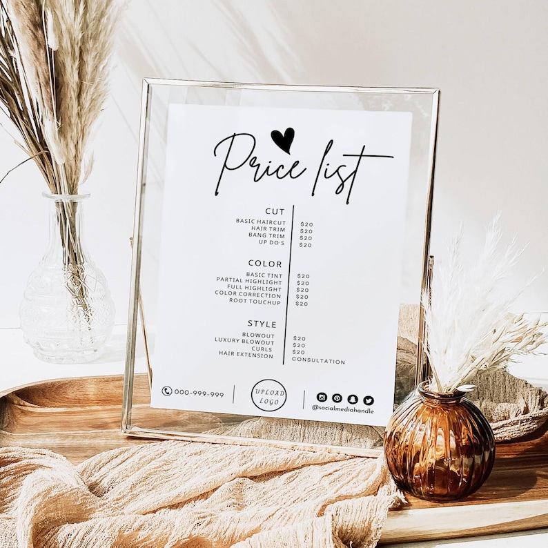 Op de afbeelding: Een witte prijslijst voor een kapsalon met een hartje en de tekst "Price list" bovenaan. De lijst bevat prijzen voor kapsels, haar knippen, kleurdiensten en stylingdiensten. De lijst is ingelijst in een zilveren lijst en staat op een houten tafel met een vaas met gedroogde bloemen en een kleine vaas met een bruine bloem.