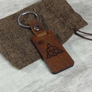 Peut inclure: Un porte-clés en bois brun avec une sangle en cuir et un anneau de clé argenté. Le porte-clés présente un motif de nœud celtique.