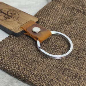 May include: A wooden keychain with a brown leather strap and a silver key ring. The wooden part has a design on it.