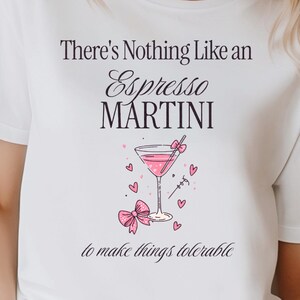 Könnte beinhalten: Weißes T-Shirt mit dem Text "There's Nothing Like an Espresso Martini to make things tolerable." Die Grafik zeigt einen rosa Martini, Herzen und eine Schleife. Das Shirt ist ein Freizeitkleidungsstück.