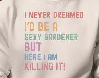 May include: White sweatshirt with the text "I NEVER DREAMED I'D BE A SEXY GARDENER BUT HERE I AM KILLING IT!" in pastel colors. The sweatshirt is worn by a person with a gold watch.
