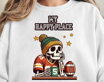 May include: White sweatshirt with a graphic of a skeleton wearing a football jersey and a beanie. The skeleton is holding a mug and a football. Text above the graphic reads "MY HAPPY PLACE" with star accents.