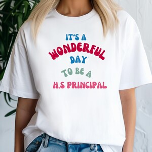 Könnte beinhalten: Weißes T-Shirt mit dem Text "It's a Wonderful Day to be a H.S. Principal" in einer Retro-Schriftart mit bunten Buchstaben.