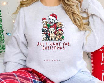 May include: A white sweatshirt with a Christmas-themed design featuring a group of dogs wearing Santa hats. The text on the sweatshirt reads "All I want for Christmas - Est 2024 - "