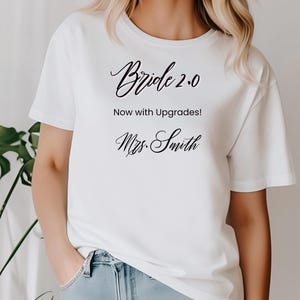 May include: White t-shirt with the text "Bride 2.0 Now with Upgrades!" and "Mrs. Smith" in black cursive font.