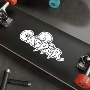 May include: A white sticker featuring the word "CASPER" in a stylized font, with the friendly ghost character peeking over the letters. The sticker is on a black surface, possibly a skateboard.