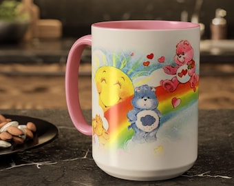 May include: A white ceramic mug with a pink handle and interior. The mug features colorful illustrations of Care Bears characters, a rainbow, and hearts. The mug is a fun and nostalgic item for fans of the Care Bears.