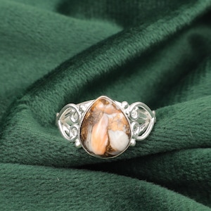 Könnte beinhalten: Ein silberner Ring mit einem tropfenförmigen braunen und weißen Edelstein, der in einem filigranen Design gefasst ist.
