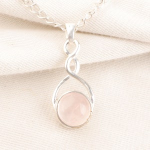 Puede incluir: Un collar de cadena de plata con un colgante de cuarzo rosa. El colgante está engastado en un diseño de nudo infinito de plata.