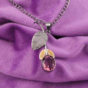 Könnte beinhalten: Eine silberne Kettenkette mit einem Anhänger in Form einer Rose mit einem violetten Edelstein und goldenen Akzenten.