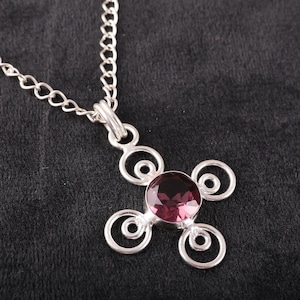 Könnte beinhalten: Eine silberne Halskette mit einem Anhänger, der mit einem violetten Edelstein in einem kreisförmigen Design besetzt ist. Der Anhänger besteht aus vier ineinandergreifenden Kreisen.