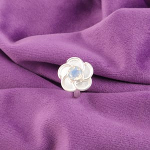 Könnte beinhalten: Ein silberner Ring mit einem Blumendesign und einem klaren Opal-Edelstein in der Mitte.