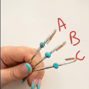 Könnte beinhalten: Drei silberne Armreifen, jeder mit einem zentralen türkisfarbenen Stein. Die Armreifen werden vor einem neutralen Hintergrund präsentiert. Die Armreifen sind mit A, B und C in rotem Marker beschriftet.