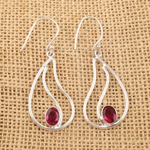 Könnte beinhalten: Ein Paar silberne Ohrhänger in Tropfenform. Jeder Ohrring hat einen einzigen, runden, dunkelrosa Edelstein.