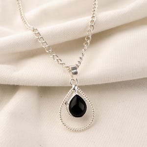 May include: A silver chain necklace with a black gemstone pendant. The pendant is shaped like a teardrop and is set in a double-loop design.