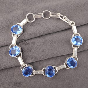 May include: A silver bracelet with five oval-shaped blue gemstones. The bracelet has a lobster clasp closure.