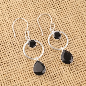 Könnte beinhalten: Ein Paar silberne Ohrringe mit schwarzen Onyx-Steinen. Die Ohrringe haben einen Kreis mit einem kleineren Kreis und einen tropfenförmigen Stein, der an der Unterseite hängt.