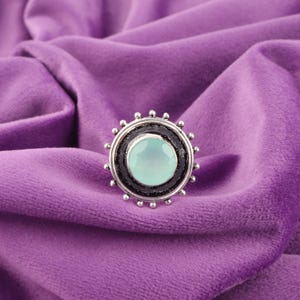 Könnte beinhalten: Ein silberner Ring mit einem hellblauen Edelstein, der in einem kreisförmigen Design mit schwarzem Hintergrund gefasst ist.