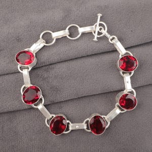 Könnte beinhalten: Ein silbernes Armband mit einem Schiebeverschluss und sechs roten Edelstein-Akzenten.