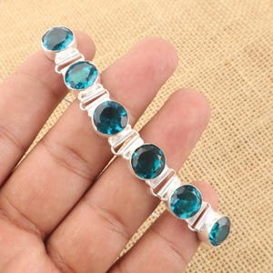Puede incluir: Una pulsera de plata con siete piedras azules redondas. La pulsera está hecha de plata de ley y presenta un diseño sencillo.