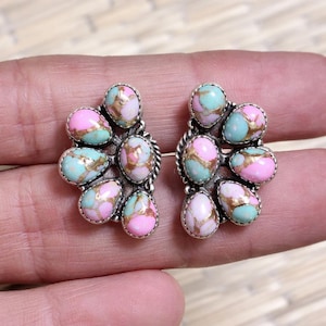 May include: A pair of silver-toned stud earrings. Each earring features a cluster of colorful, oval-shaped stones in shades of pink, turquoise, and gold. The stones are set in a silver metal with a textured border, creating a unique and eye-catching design.