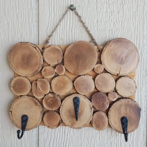 May include: Wooden key holder with three hooks. The holder is made of wood slices arranged in a rectangular shape. The hooks are black metal.
