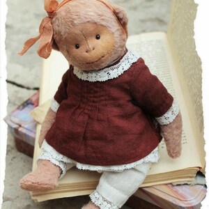 May include: A plush monkey doll wearing a burgundy dress with white lace trim and a white lace-trimmed underskirt. The monkey has a peach-colored bow in its hair and is sitting on a stack of old books.