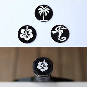 May include: Three black round stickers with white designs. The designs are a palm tree, a hibiscus flower, and a seahorse. A black bottle stopper with a white hibiscus flower design.