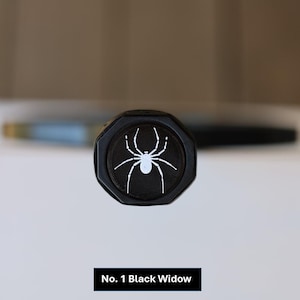 May include: Black octagonal object featuring a white spider design. The text "No. 1 Black Widow" is at the bottom. A blurred pen is in the background.