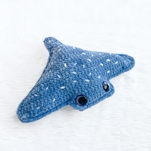 May include: A handmade blue plush stingray toy with white speckles and large, dark blue button eyes. The soft toy is made of a textured material and is designed in a stylized shape, perfect for children's play or as a decorative item.