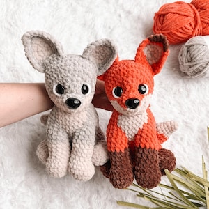 May include: Two handmade crochet stuffed animals: a gray mouse and an orange fox. The fox has white and brown accents. Both have large black eyes and are sitting. Orange and gray yarn balls are in the background.