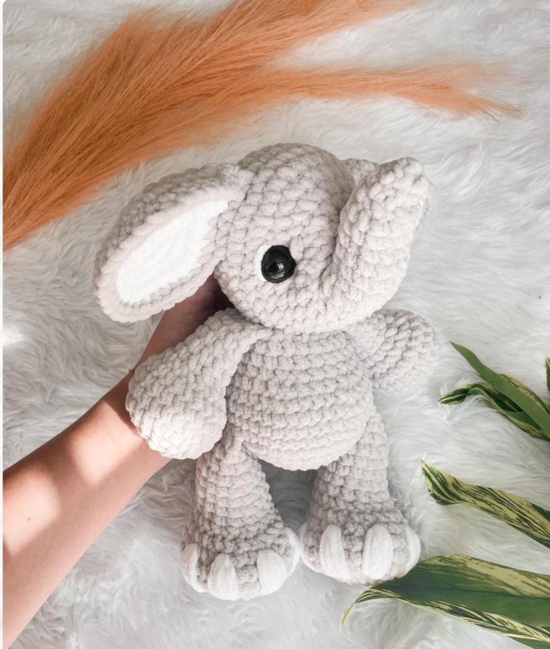 May include: A handmade gray crochet elephant plush toy with large ears and black eyes. The elephant is soft and cuddly, perfect for a child's room or nursery. The plush toy is made with a textured yarn.
