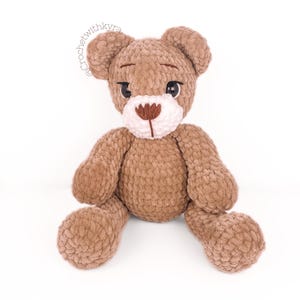 Peut inclure: Un ours en peluche crochet&eacute; marron avec du fil blanc pour le nez et des yeux en boutons noirs. L'ours est assis les jambes &eacute;cart&eacute;es.