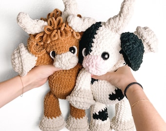 May include: Two crocheted stuffed cows, one brown and one black and white. The brown cow has a curly mane and both cows have large black eyes.