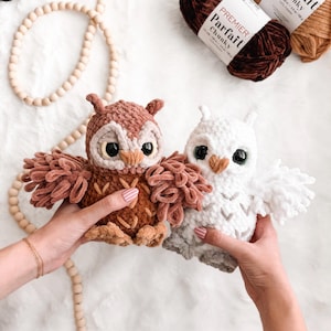 May include: Two handmade crochet owl plushies, one brown and one white, with large black eyes and fluffy wings. The brown owl has a light brown chest and the white owl has a gray chest. Yarn skeins in brown and tan are in the background.