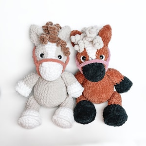 May include: Two crocheted stuffed horses, one gray and one brown, with pink and black details. The horses have fluffy manes and tails.