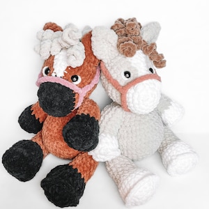 May include: Two crocheted plush horse toys. One is brown with black hooves and a pink nose, the other is gray with white hooves and a pink nose.