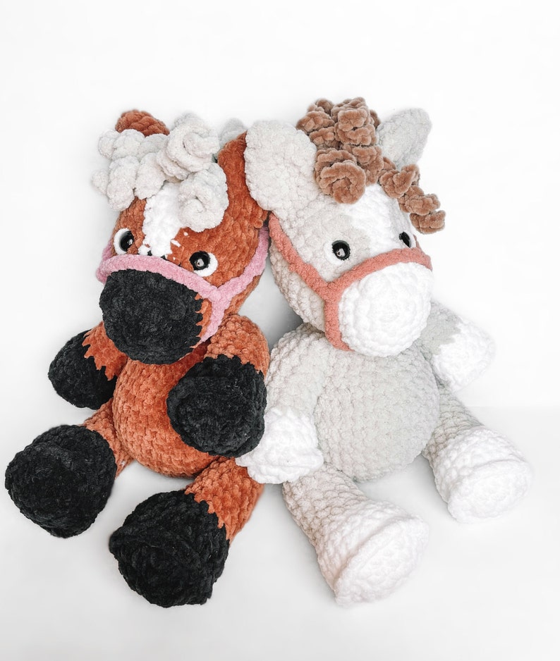 May include: Two crocheted plush horse toys. One is brown with black hooves and a pink nose, the other is gray with white hooves and a pink nose.