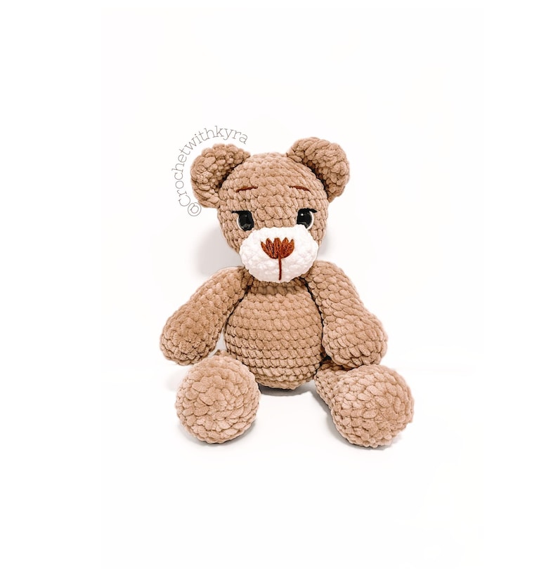 Peut inclure: Un ours en peluche crochet&eacute; marron avec des traits du visage brod&eacute;s en blanc et marron. L'ours est assis les jambes &eacute;cart&eacute;es.