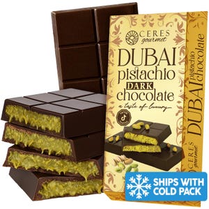 May include: Dark chocolate bars with pistachio filling are stacked next to a package of Dubai pistachio dark chocolate. The packaging is gold and features the Ceres Gourmet logo and the words "Dubai Pistachio Dark Chocolate".
