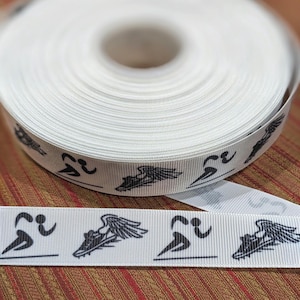 May include: White ribbon featuring a repeating pattern of a running figure and a winged running shoe in black. The ribbon is rolled up, with a section unrolled to show the design. The background is a reddish-brown fabric.