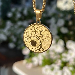 May include: A gold necklace with a pendant featuring a tree of life design with a sun and moon on either side.