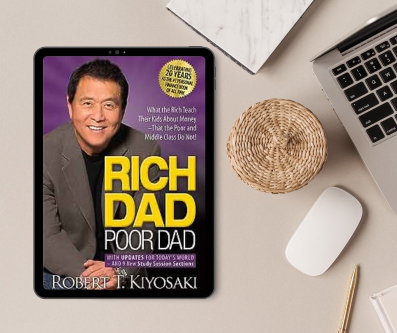 Puede incluir: Una tableta muestra la portada de "Rich Dad Poor Dad" de Robert T. Kiyosaki. La portada presenta una foto del autor y el t&iacute;tulo en amarillo. La tableta est&aacute; sobre un escritorio con un port&aacute;til, un rat&oacute;n y un posavasos tejido.