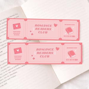 Könnte beinhalten: Zwei rosa "Romance Readers Club" Lesezeichen mit Ticket-Design. Jedes Lesezeichen zeigt einen Umschlag, Sterne, ein Herz und eine Buchillustration. Die Lesezeichen liegen auf einem offenen Buch.