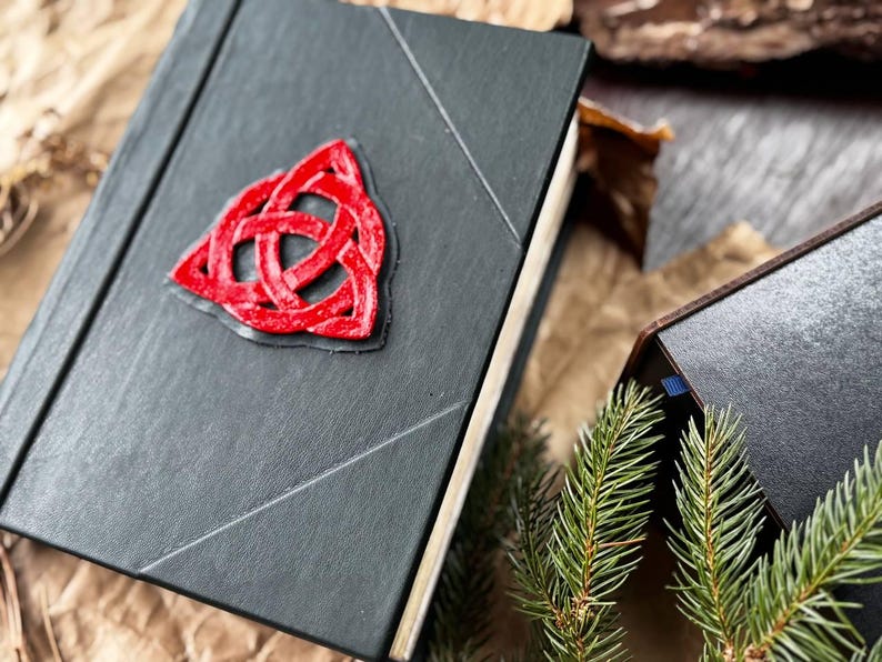 May include: A black leather-bound journal with a red three-dimensional Celtic knot design on the front cover.