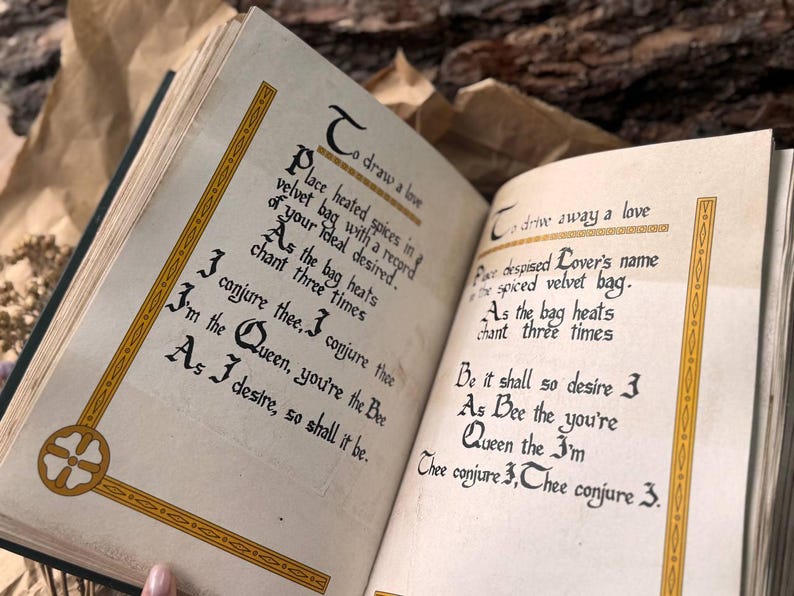 May include: An open book with yellowed pages and gold trim. The text on the pages is in a handwritten font and reads "To draw a love" and "To drive away a love". The text describes a spell using a velvet bag and heated spices.